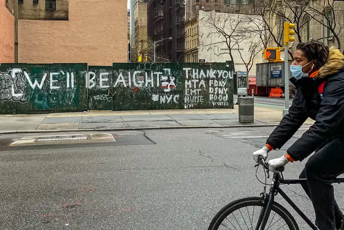 A bike rider passes by graffiti that says "We'll be aight"
